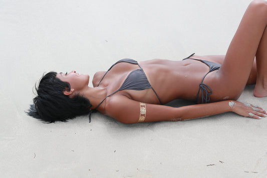 Woman lying on white sand wearing the BUNNIES ROOM Miami Bikini in Graphite.